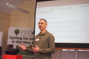A man stands in front of a screen presenting and making hand gestures.