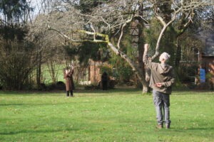 Two people stand in a field with a tree looking to the sky taking part in a nature connection session.