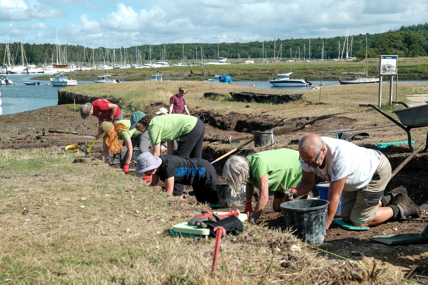 A line of volunteers kneel in a trench in the earth during an archaeological dig at Buckler's Hard.