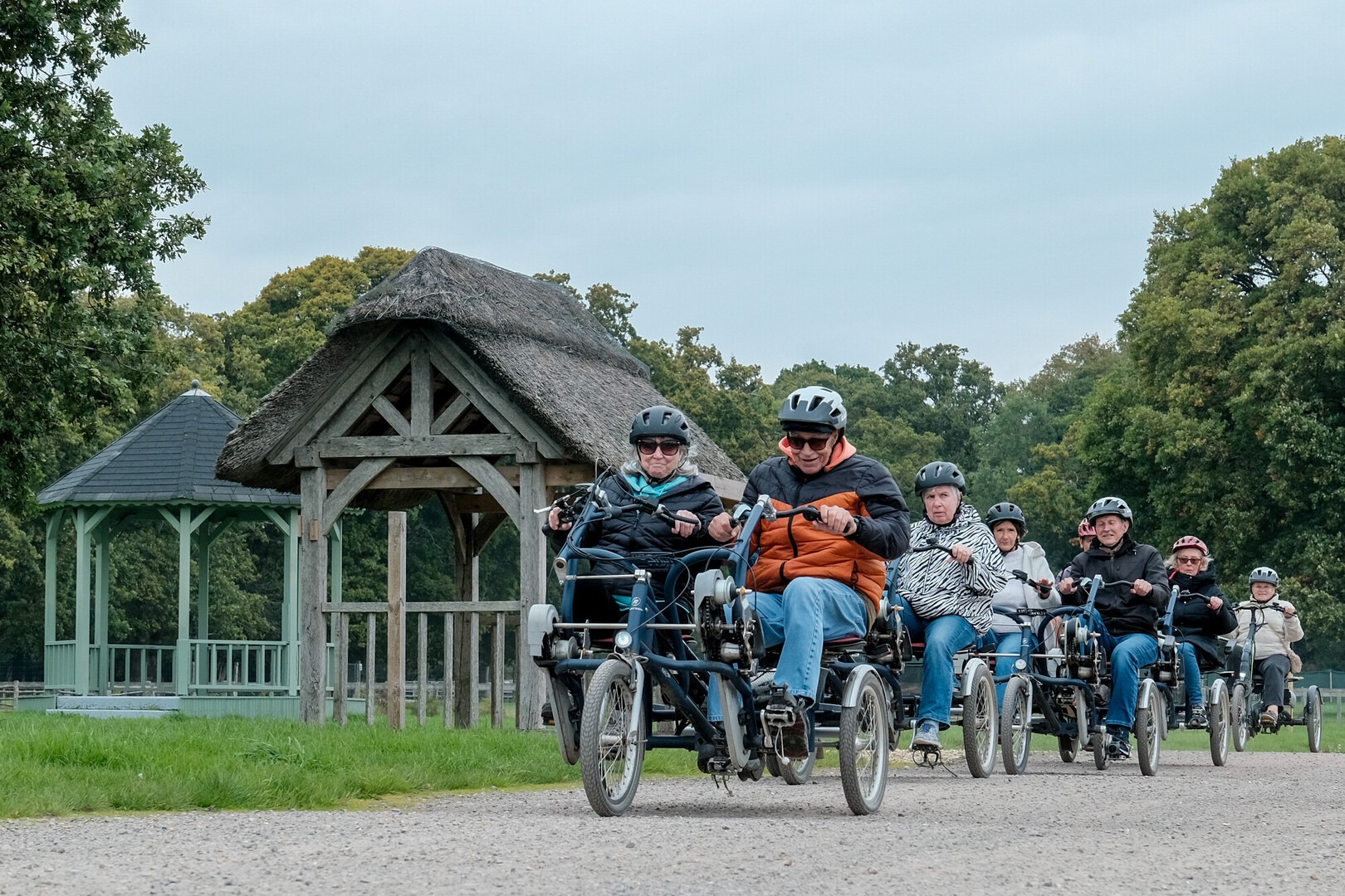 Riders on a series of adapted cycles on a New Forest track with a wooden building in the background.