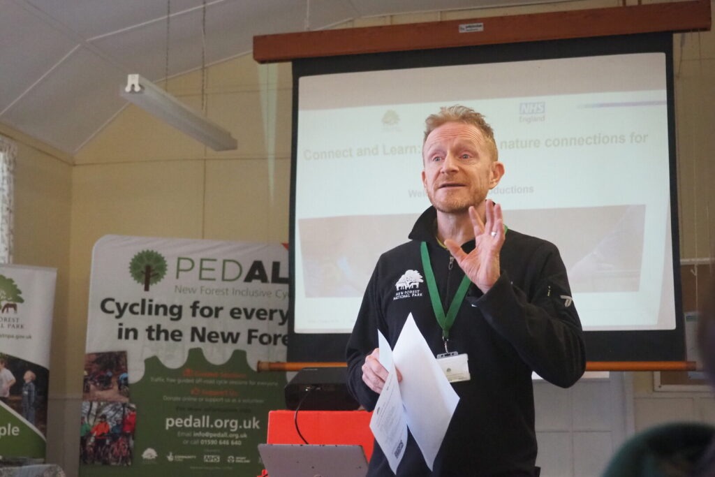 A man stands in front of a projector screen giving a talk about health and wellbeing in the New Forest.