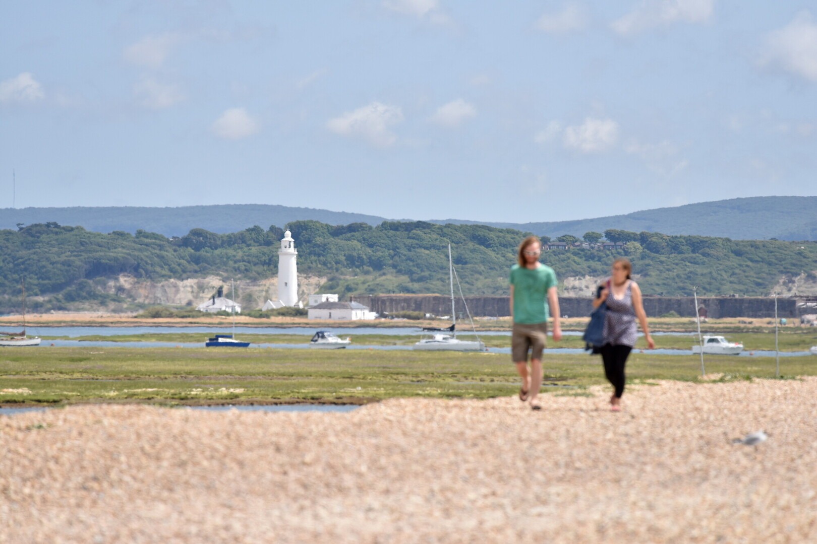 Two walkers on the coast at Hurst Spit with heathland in the background and shingle in the foreground.