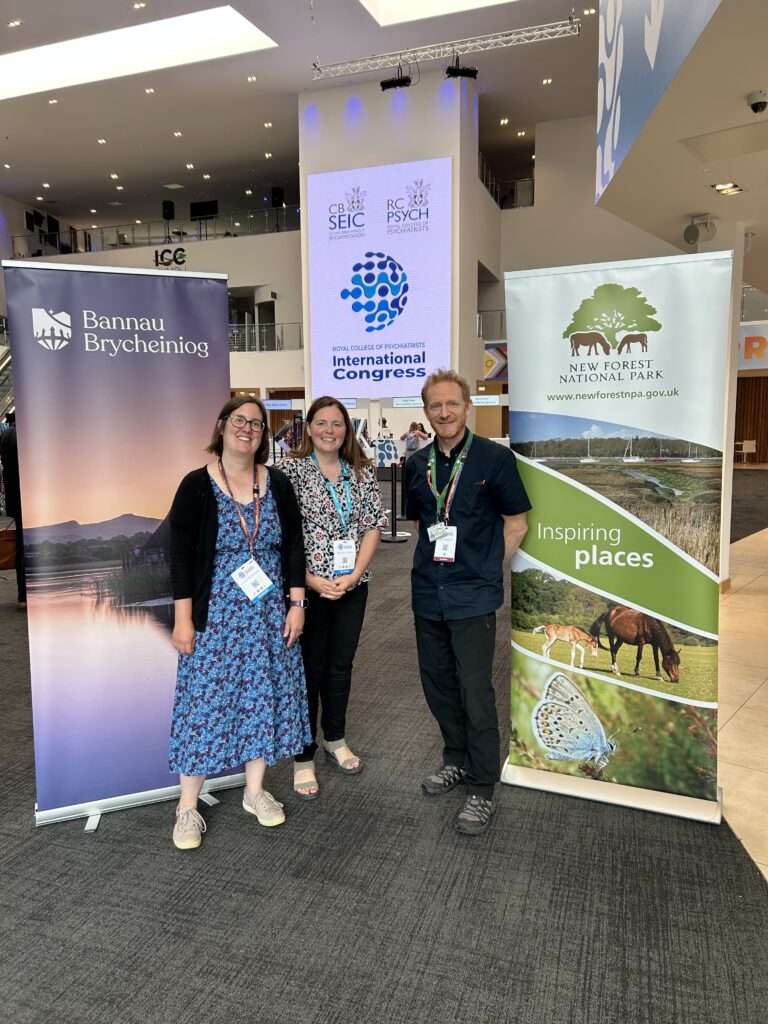 Three people stand at a medical conference event in a foyer with national park banners between them.